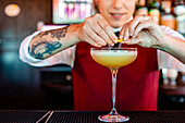 Crop female bartender garnishing sour cocktail in glass placed on counter in pub