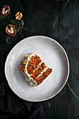 Top view of yummy cake with cream cheese served on plate with fresh carrot slices and walnuts
