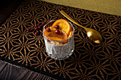 High angle of glass of dessert made of stracciatella mousse and shavings of chocolate topped with caramelized slices of orange and berries near spoon