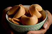 Closeup hands of anonymous woman holding small bowl full of crispy fortune cookies