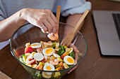 Crop female putting fresh shrimps on top of salad in glass bow in kitchen at home