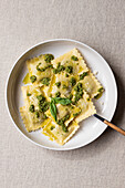Draufsicht auf appetitliche gekochte Ravioli mit grüner Soße und Kräutern auf weißem Teller mit Gabel auf dem Tisch