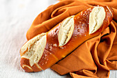 From above fresh salty pretzel baguette placed on orange cloth on white background