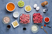 From above fresh chopped vegetables and raw minced meat placed on table with seasonings and sauces