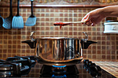 Anonyme Person mit leckerer Feigenmarmelade auf einem Spatel über einem Schnellkochtopf auf einem Gasherd in der Küche