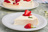Slice of tasty sweet baked cheesecake with ripe strawberries served on white plate on table in light kitchen