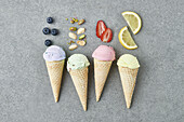 Top view of assorted appetizing ice cream cones with blueberry pistachio walnuts strawberry and lemon composed on gray table with ingredients in kitchen