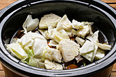 From above of pieces of chopped cabbage and vegetables cooking in slow cooker while preparing for corned beef