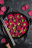 Top view composition of tasty beetroot slices arranged on baking pan with green jalapeno peppers and placed on black towel on kitchen table close to chopsticks
