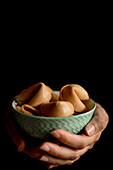 Closeup hands of anonymous woman holding small bowl full of crispy fortune cookies