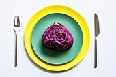 From above of halved red cabbage placed on yellow and green plates on white background