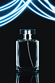 Composition of stylish perfume bottle with lid placed on black background near blue luminous illumination