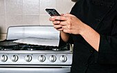Crop unrecognizable female chef in uniform browsing on smartphone in modern kitchen in restaurant