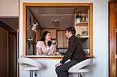 Positive multiracial couple with hot drinks looking at each other while having conversation at counter in modern kitchen at home