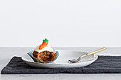 Halb gegessener Karotten-Cupcake mit Sahne auf einem Teller vor weißem Hintergrund