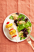 Top view of fresh vegan plate with vegetable skewer and marinated tofu served with a mixed lettuce salad