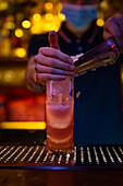 Hände eines nicht erkennbaren Barkeepers, der bei der Zubereitung eines Cocktails in der Bar zerstoßenes Eis in einen Becher gibt