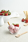 Delicious homemade strawberry ice cream scoops served in glass bowl with berries and waffle roll in kitchen in daylight
