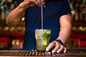 Unrecognizable bartender holding the glass and stirring mojito cocktail in the bar