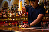Young Asian bartender pouring lemon juice in the glass while preparing mojito cocktail in the bar