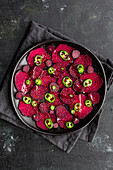 Top view composition of tasty beetroot slices arranged on baking pan with green jalapeno peppers and placed on black towel on kitchen table