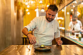 Mann gießt flüssigen Stickstoff aus einer Sauciere auf einen Teller mit Seeigel in einem Restaurant für Molekularküche
