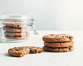 Abundance of delicious sweet cookies with chocolate chips placed on white table with glass jar on white background in light kitchen