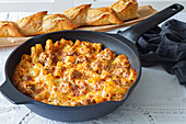 Appetizing gratin macaroni with meatballs and tomato sauce with mozzarella cheese prepared and served in skillet on table with fresh crusty bread