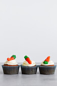Rows of sweet delicious carrot cupcakes with tender cream and carrot shaped gummies on gray surface