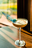 Creative fancy bright yellow alcoholic drink served in cocktail glass on wooden bar counter