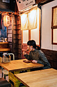 Young Asian woman in sweater eating at wooden counter in cafe