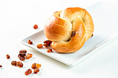 From above delicious twisted bun served with sweet raisins on rectangular plate on white background