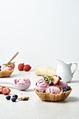 Yummy berry ice cream scoops on crispy waffle bowl decorated with fresh ripe strawberries blueberries pistachio and mint leaves against white background
