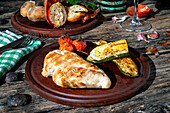 Tasty grilled chicken breast served on plate with fresh roasted cherry tomatoes and zucchini placed on wooden table with onion