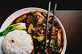 Draufsicht auf appetitlich gekochte Yuxiang-Aubergine mit gesundem Gemüse und Reis auf einem weißen Teller in einem asiatischen Restaurant
