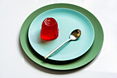 From above of appetizing red berry jelly placed on pale blue round plate with spoon on white surface