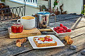 Teller mit leckerem Toast und Himbeeren neben einer Tasse Tee und einer Teekanne aus Metall auf einem Holztisch auf der Terrasse bei Tag