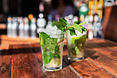 Glasses of refreshing mojito cocktails with ice and mint served on outdoor wooden bar counter