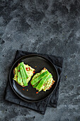 Appetitliche Toasts mit frischer Guacamole und grünen Erbsenschoten garniert auf einem schwarzen Teller