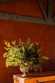 Vase mit frischem grünem Laub auf einem Holztisch auf der Terrasse im Sonnenlicht
