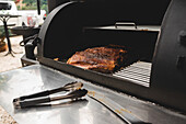 Delicious grilled pork ribs with crust placed on metal rack in modern barbecue grill machine with racks in light cafe