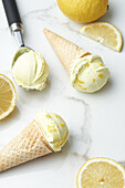 Waffeltüten und Kugel mit köstlichem hausgemachtem Eis auf einem Marmortisch mit Zitronenscheiben im Tageslicht von oben