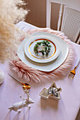 From above christmas table settings with a wreath decoration with white and golden dinnerware on fluffy placemat on pink tablecloth