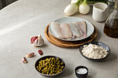 Von oben: Frische Knoblauchzehen und Salz auf dem Tisch neben Seehechtfilet, Schüssel mit Erbsen und Mehl bei der Zubereitung von Speisen in der Küche