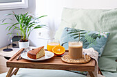 Cup of coffee and homemade sponge cake placed on wooden tray with glass of fresh orange juice prepared for breakfast in bedroom