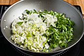 Fresh chopped green onion frying in metal pan on modern black cooker during cooking process in light kitchen at home