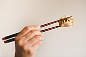 Hand of woman holding chopsticks with tasty steamed dumpling on grey background