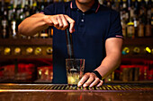 Unrecognizable bartender crushing lemon wedges in the glass while preparing mojito cocktail in the bar