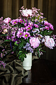Strauß frischer bunter Pfingstrosen und Chrysanthemen in weißer Vase auf Holztisch in dunklem Raum