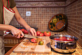 Seitenansicht einer ethnischen Frau in Schürze, die reife Tomaten auf einem Schneidebrett schneidet, während sie das Mittagessen in der Küche zu Hause zubereitet